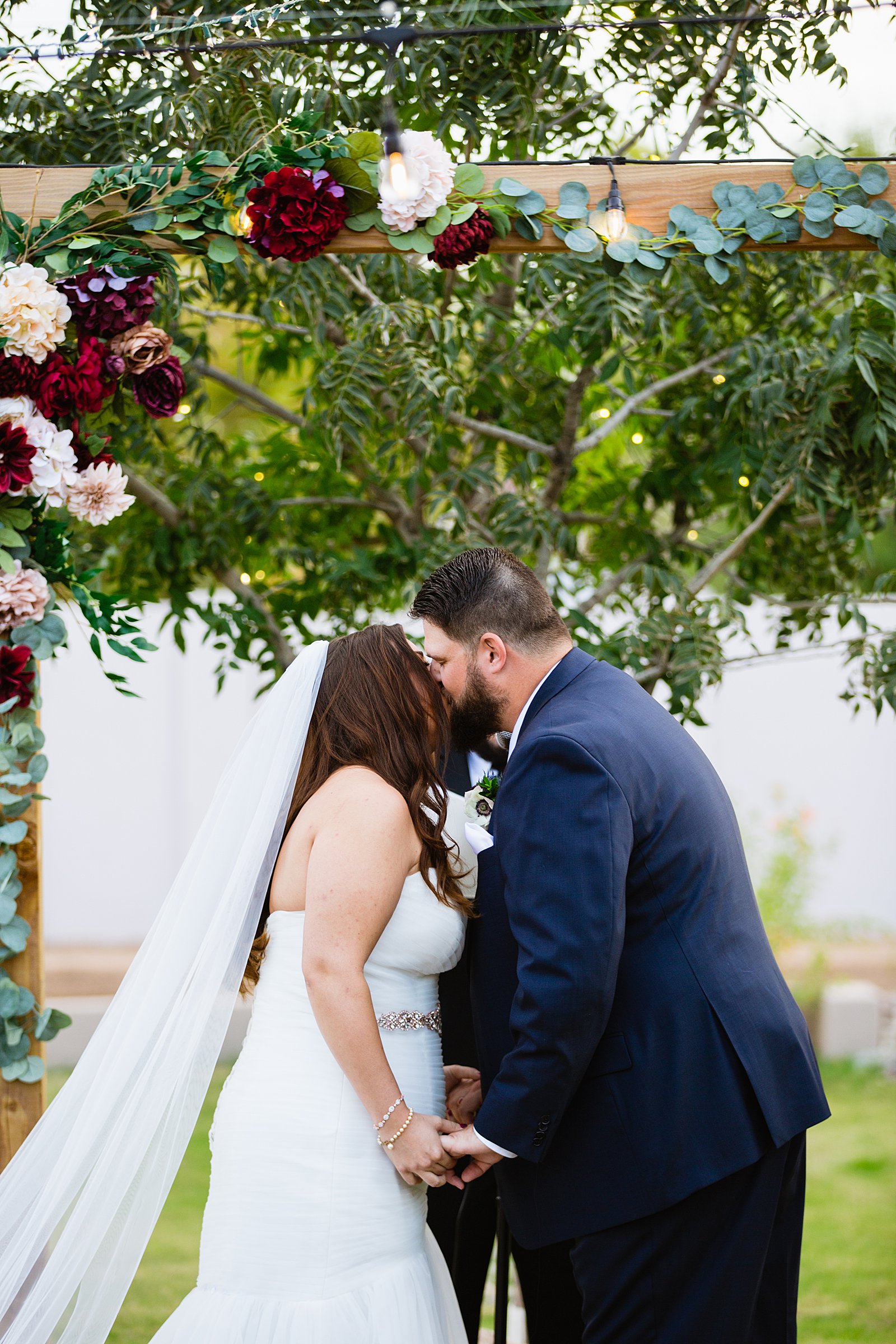 Bride and Groom share their first kiss during their wedding ceremony at an Arizona backyard by Arizona wedding photographer PMA Photography.