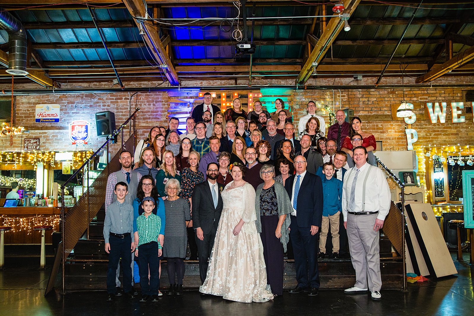 Bride and groom pose with all guests at their wedding reception at The Duce by PMA Photography.
