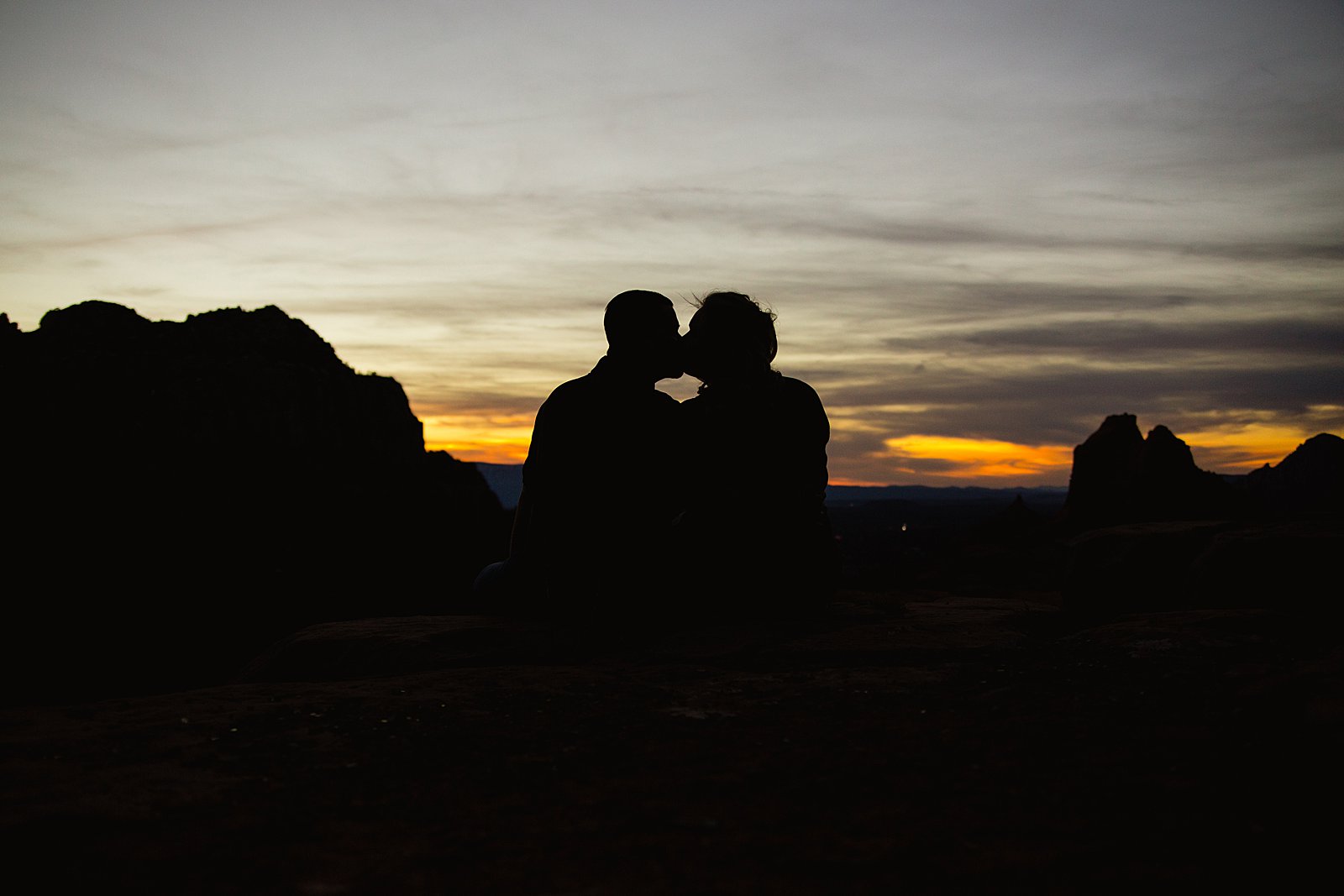 Couple share a kiss at sunset during their Merry Go Round Rock engagement session by Sedona wedding photographer PMA Photography.
