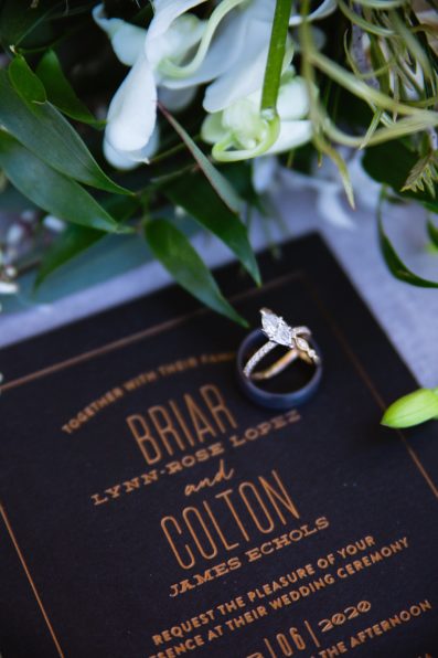 Bride's unique gold marquise wedding ring and groom's black wedding band on black and copper wedding invitations by PMA Photography.