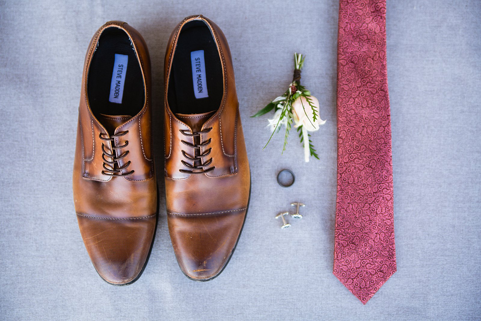 Groom's wedding day details of tan shoes, boutonniere, wedding band, cufflinks, and red copper tie by PMA Photography.