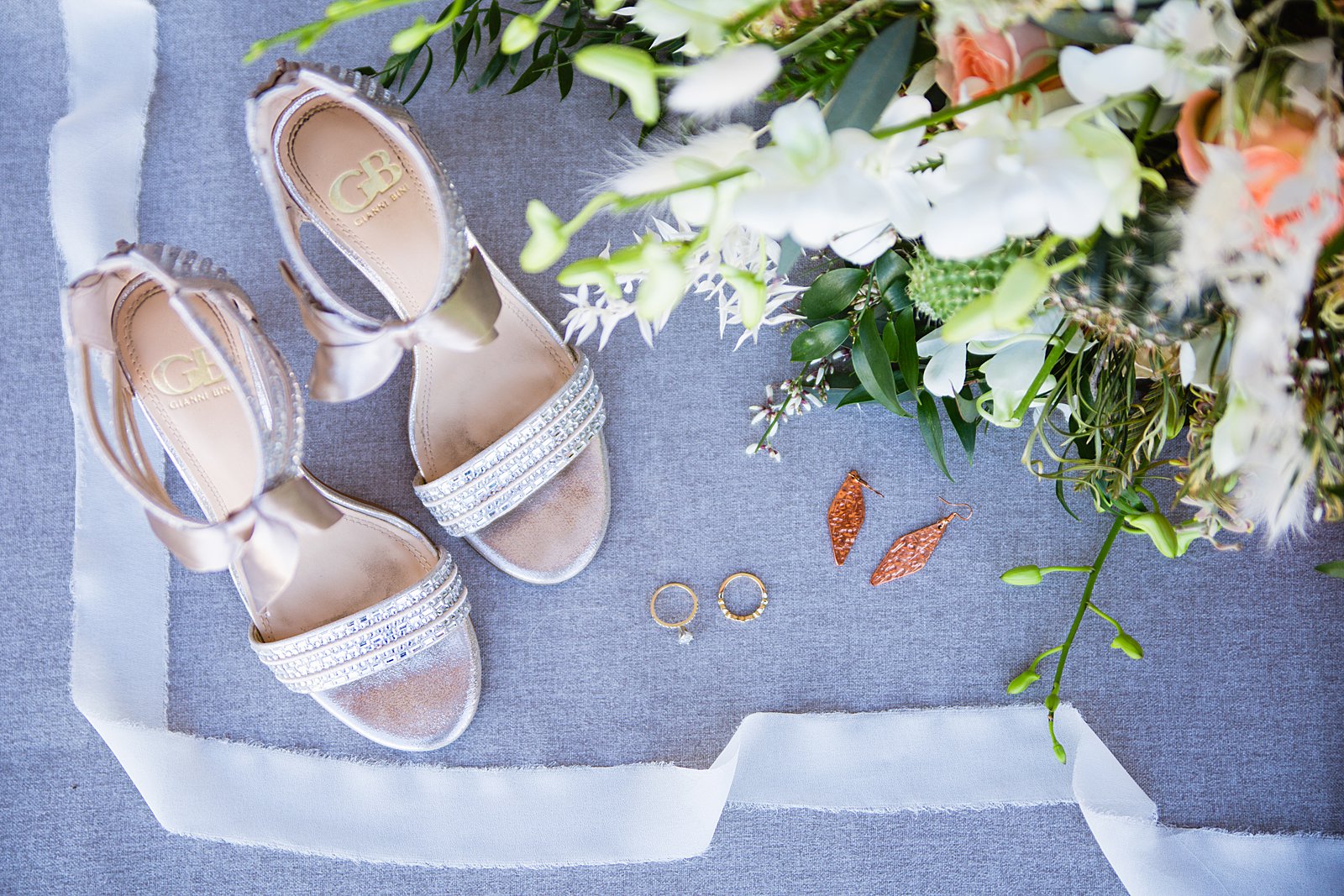 Brides's wedding day details of cream shoes, wedding ring, copper earrings, and bouquet by PMA Photography.