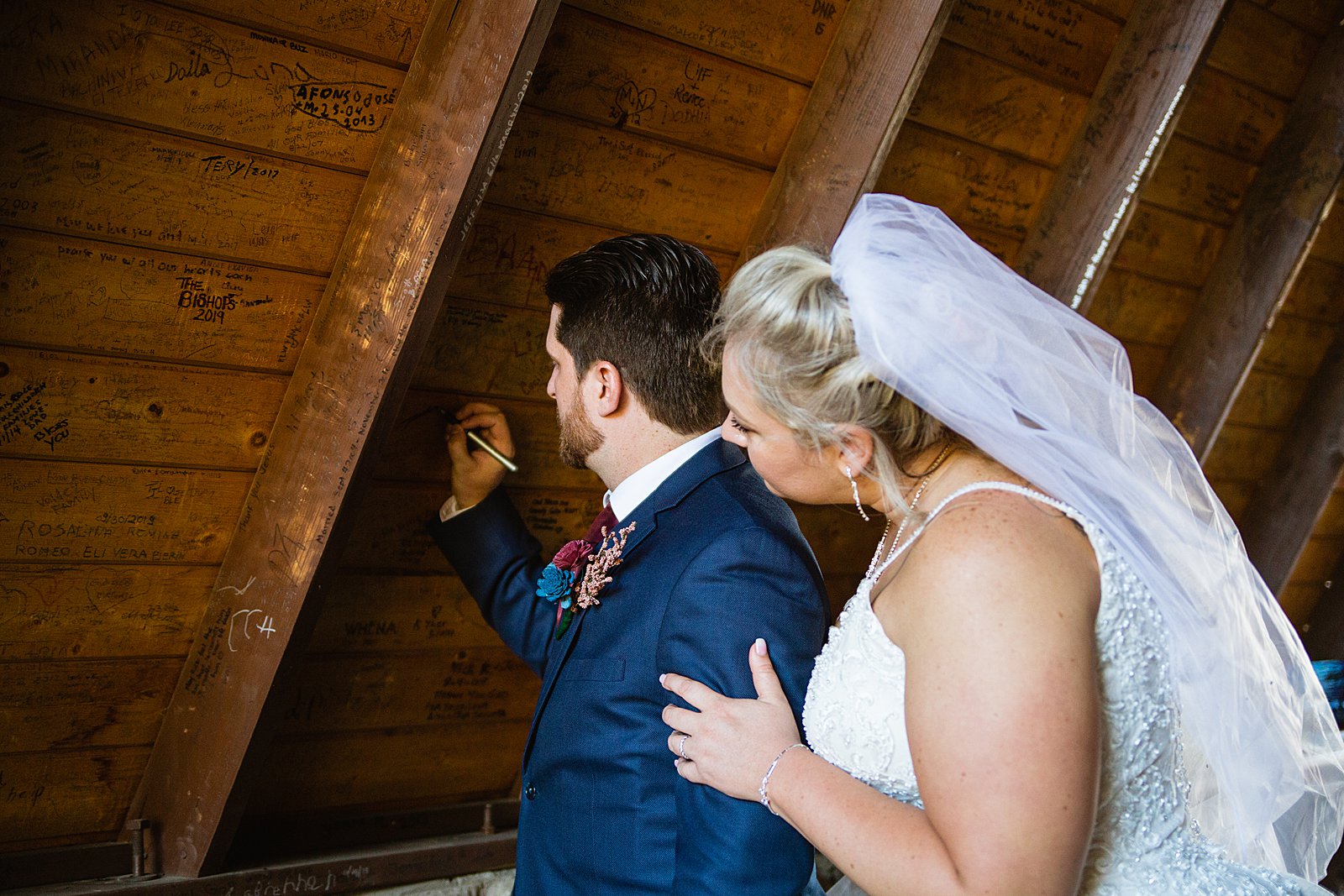Bride and groom sign their names and wedding date on the walls of the Chapel of the Holy Dove by Arizona wedding photographers PMA Photography.