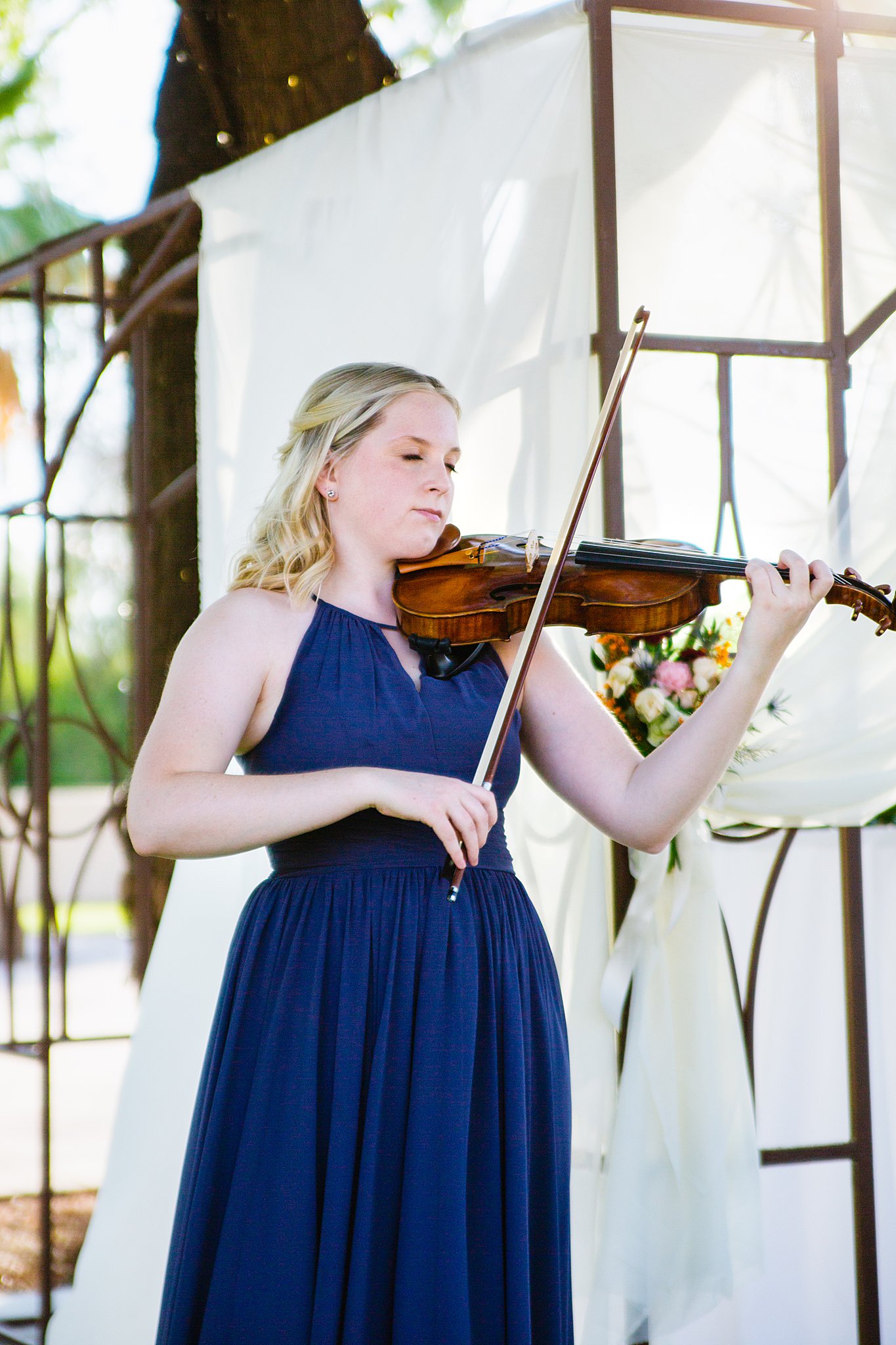 Bridesmaid plays violin as the wedding party walks down the aisle during a Secret Garden Events wedding by Arizona wedding photographer PMA Photography.