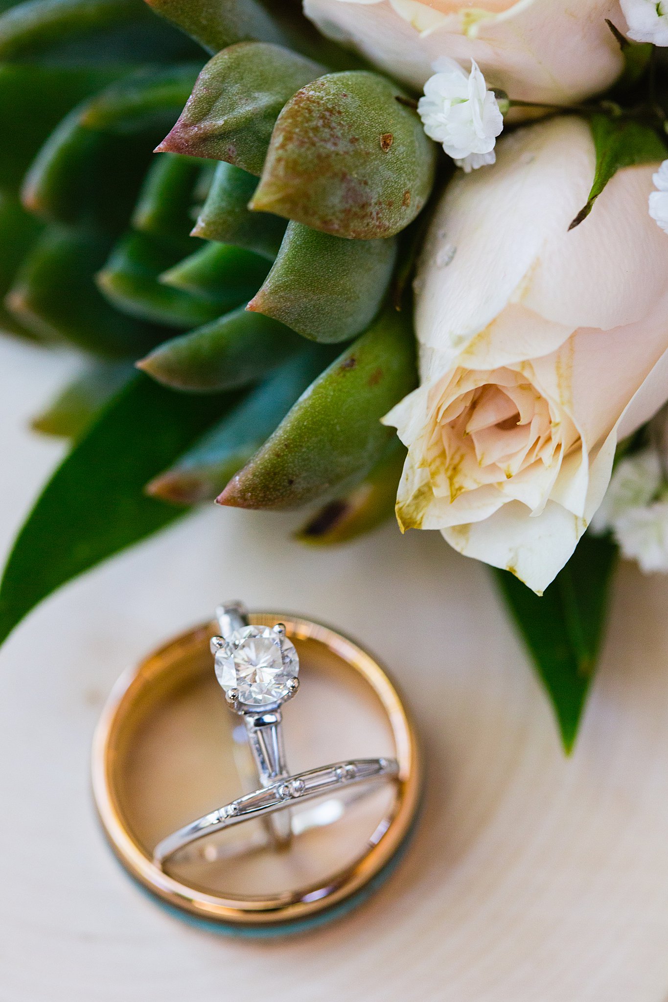 Bride and groom's wedding rings with a succulent and pink rose by PMA Photography.