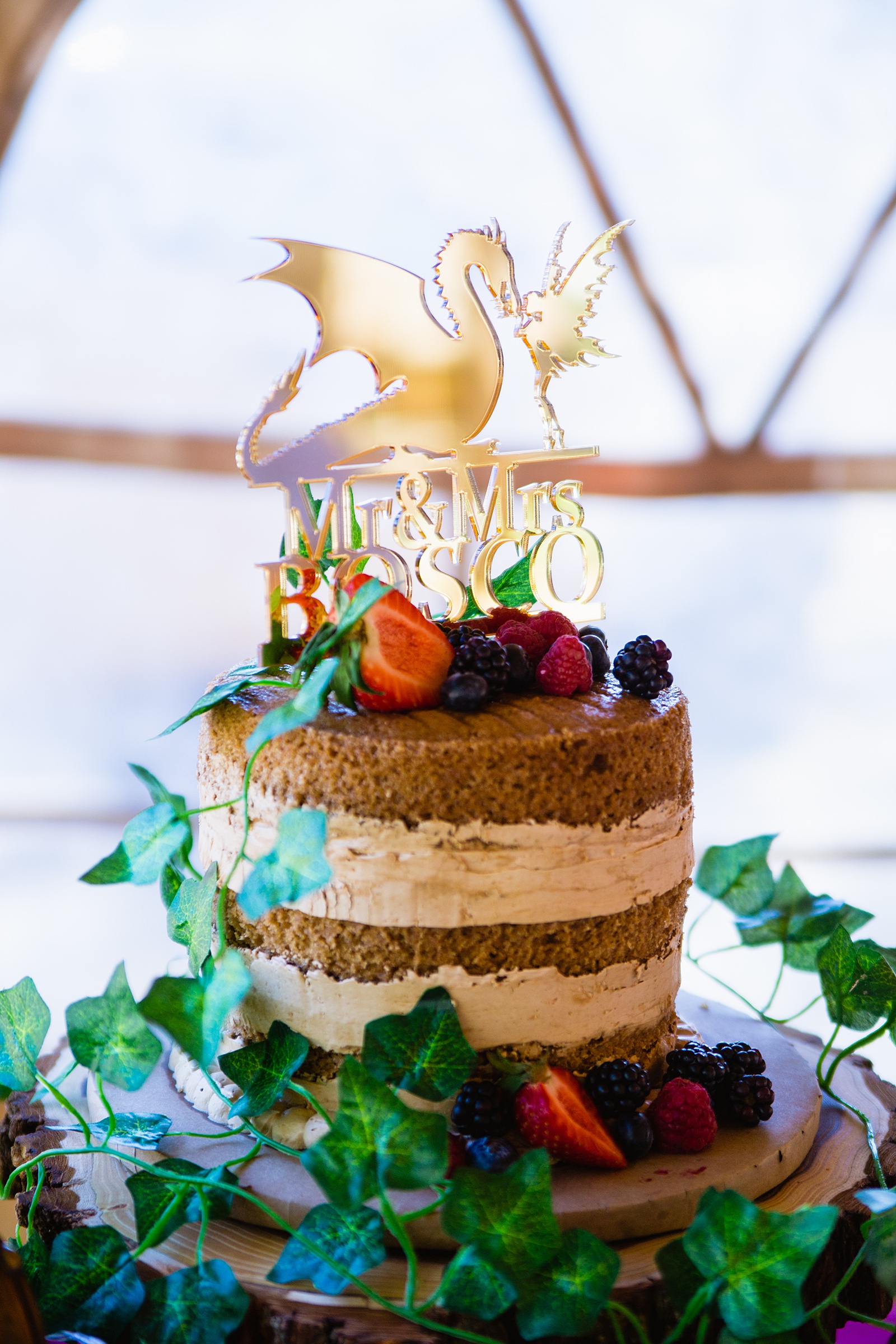 Naked cake with fresh berries and a fantasy inspired cake topper with dragon and fairy by Arizona wedding photographer PMA Photography.