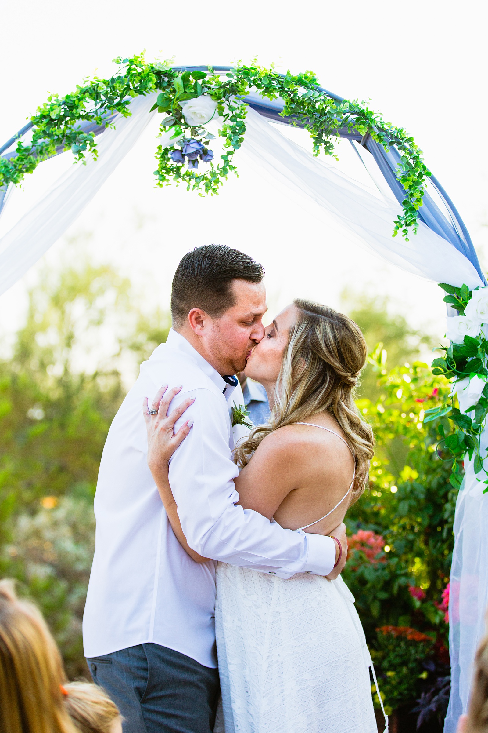 Bride and Groom share their first kiss during their wedding ceremony at a backyard by Arizona wedding photographer PMA Photography.