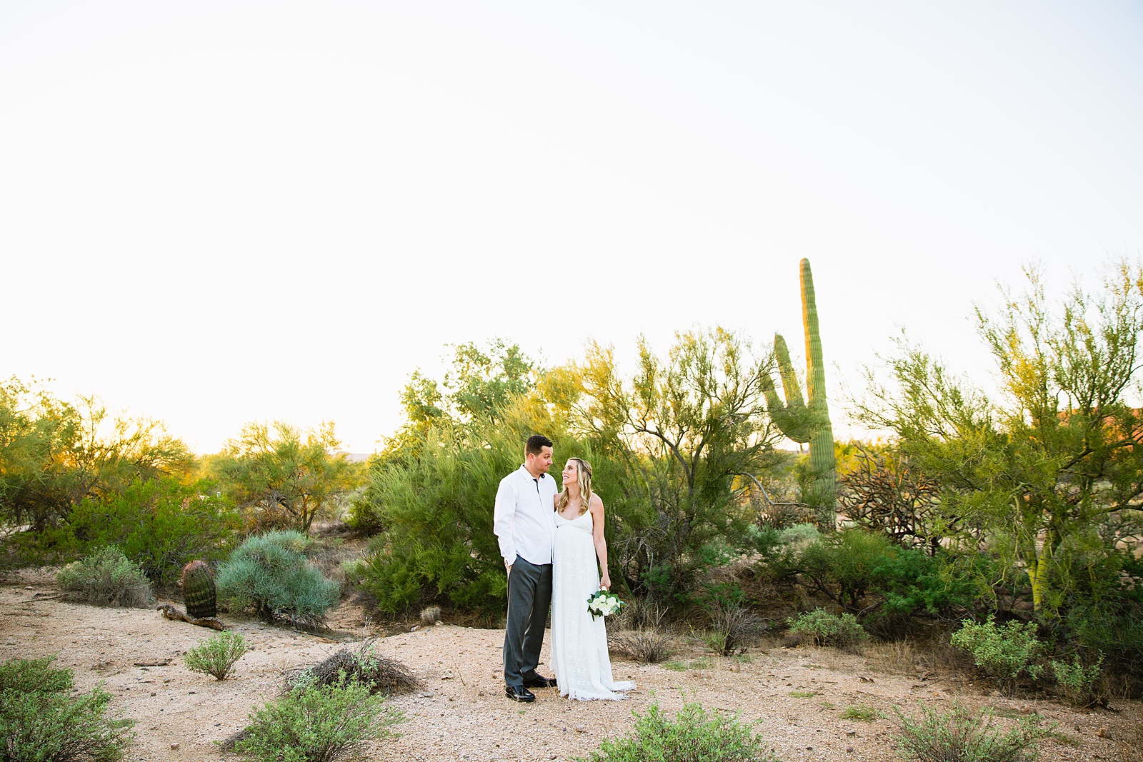 Pregnant bride and Groom pose together during their desert backyard elopement in Scottsdale by Arizona wedding photographer PMA Photography.