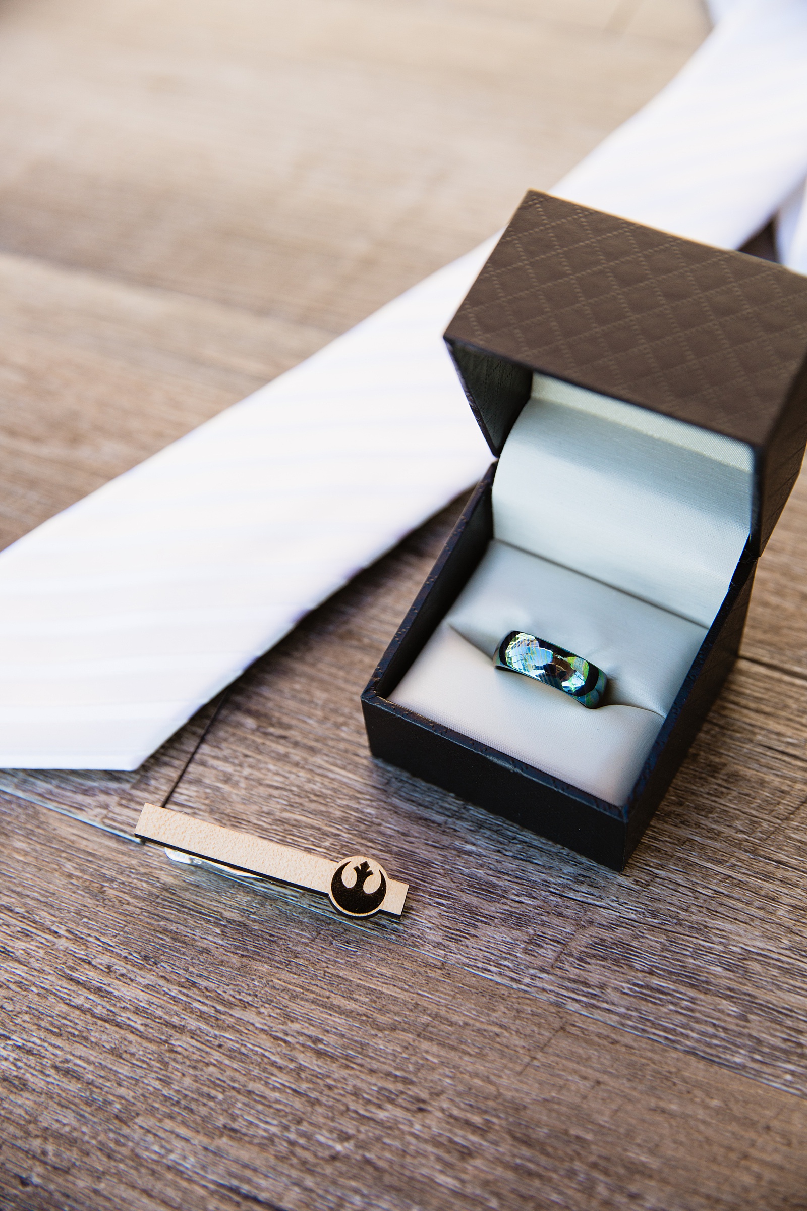 Grooms wedding day details with a white tie, Star Wars tie clip, and blue metal wedding band by Phoenix wedding photographer PMA Photography.
