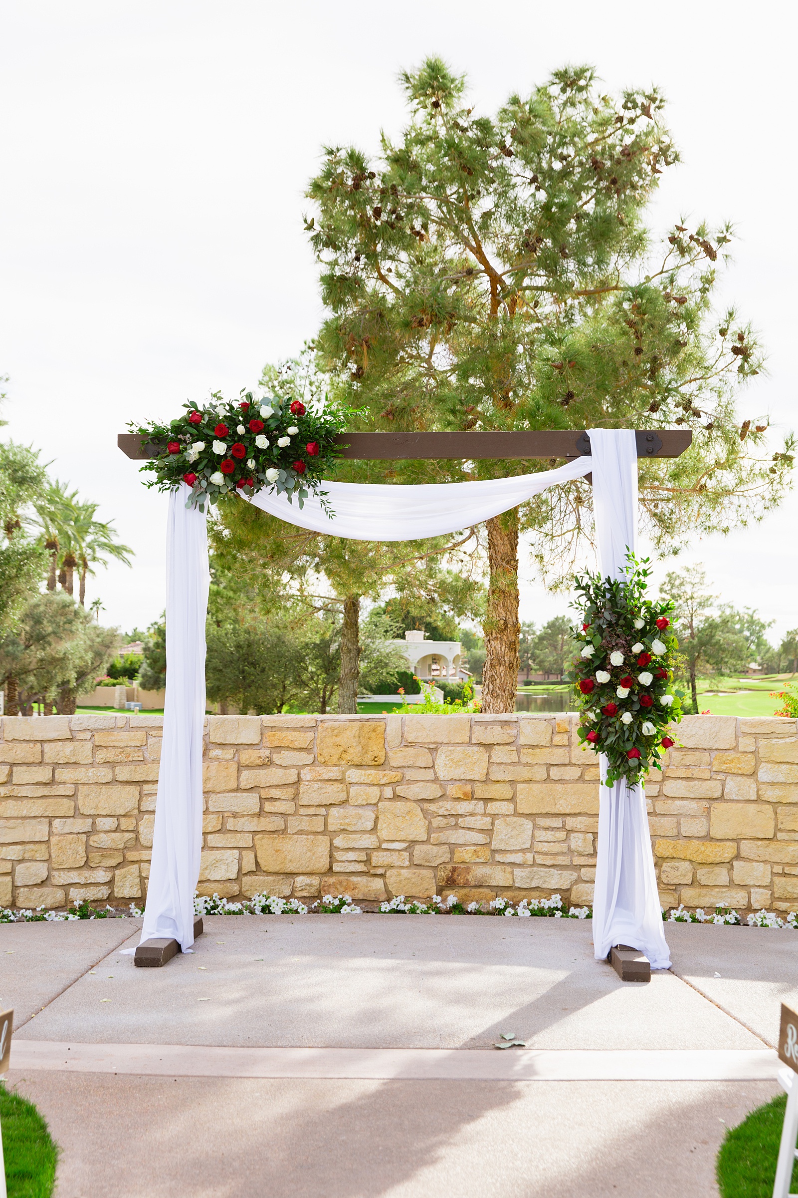 Wedding ceremony arch with red and white roses at Ocotillo Oasis by Phoenix wedding photographer PMA Photography.