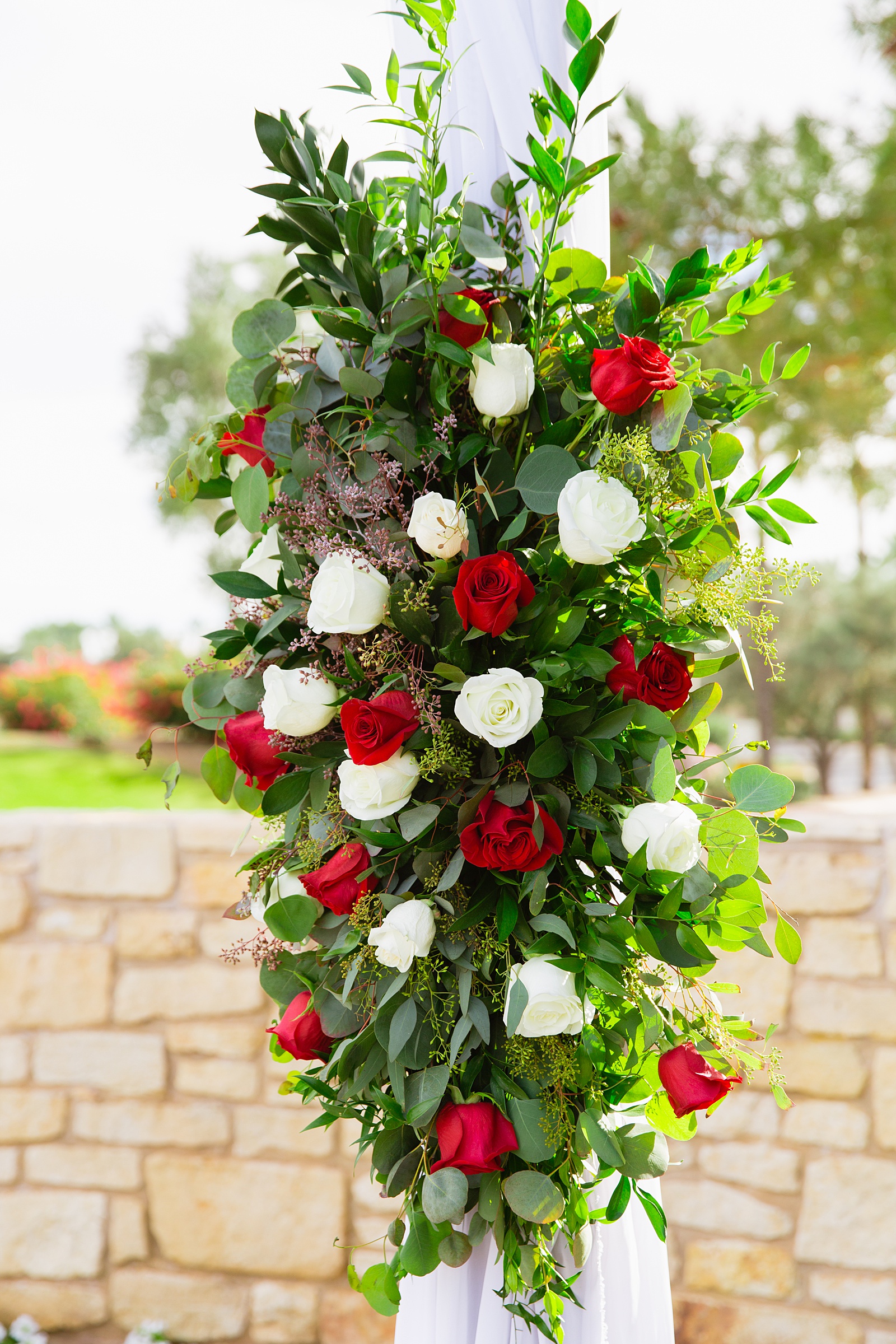 Wedding ceremony arch florals with red and white roses at Ocotillo Oasis by Phoenix wedding photographer PMA Photography.