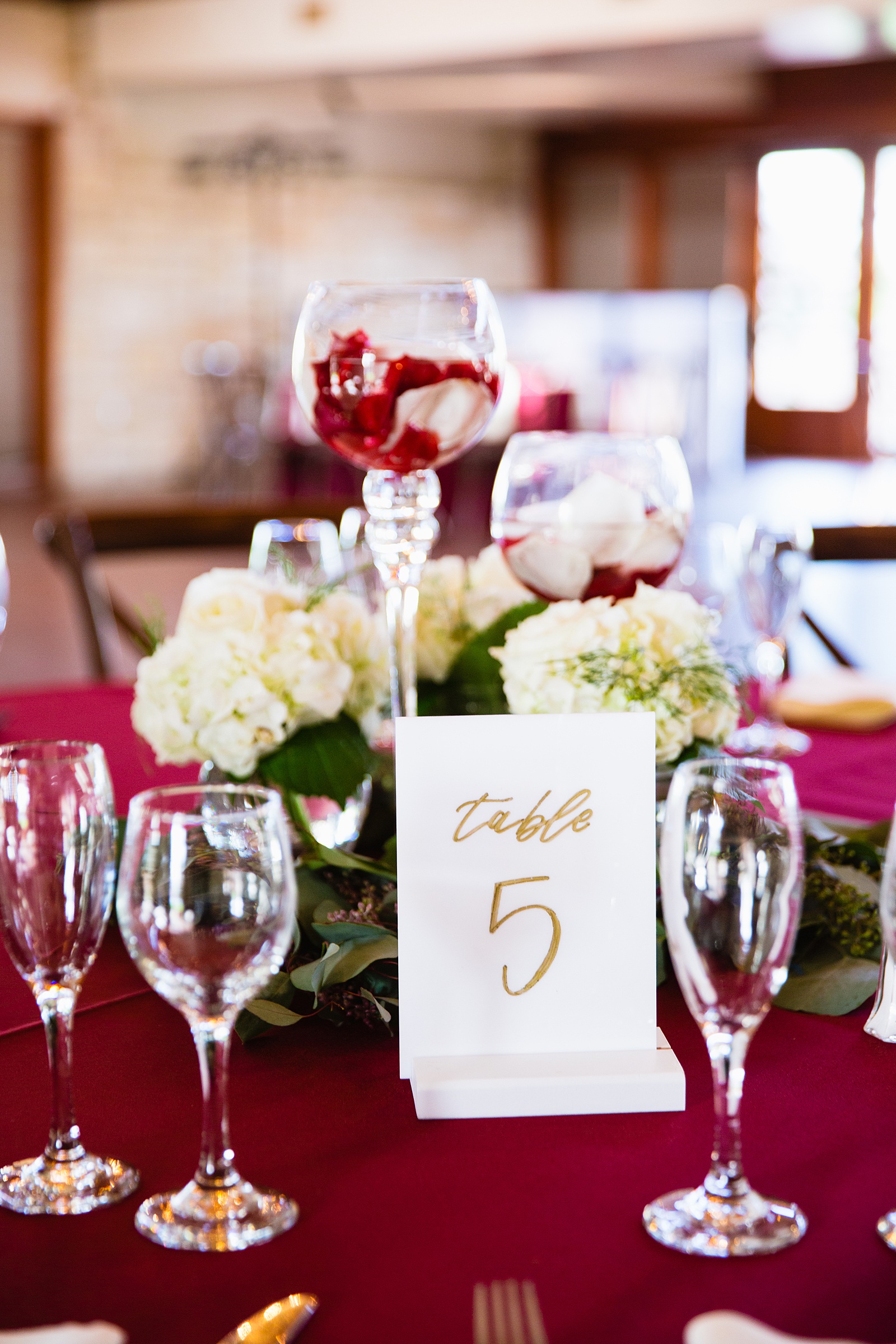 Gold calligraphy white table numbers with red and white flowers centerpieces at Ocotillo Oasis wedding reception by Phoenix wedding photographer PMA Photography.