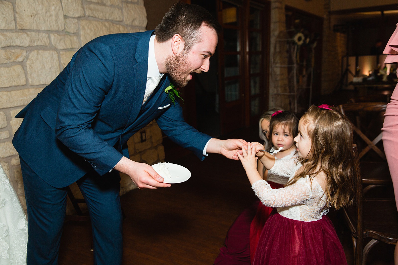 Candid photo of the groom sharing cake with the flower girls at an Ocotillo Oasis wedding reception by Arizona wedding photographer PMA Photography.