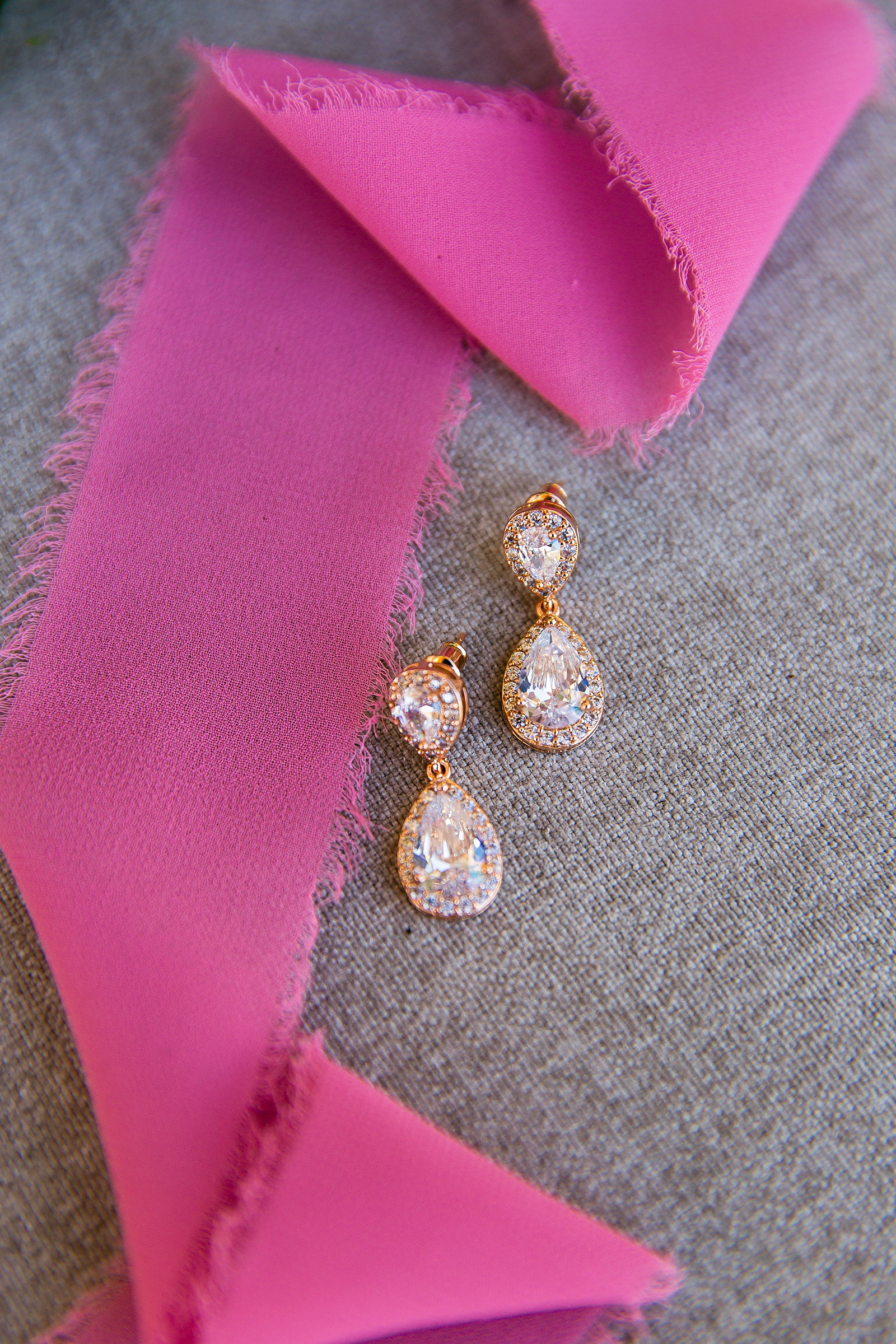 Bride's gold teardrop earrings with a pink ribbon by Arizona wedding photographer PMA Photography.