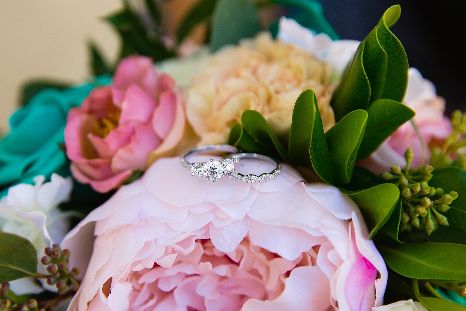 Bride's white gold and diamond wedding band and engagement ring set on top of a pink and teal wedding bouquet by Arizona wedding photographer PMA Photography.