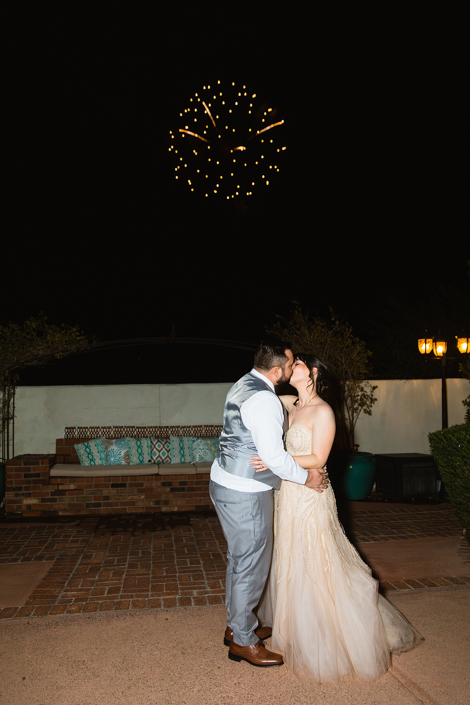 Bride and Groom share a kiss while fireworks go off in the sky during their Bella Rose Estate wedding by Arizona wedding photographer PMA Photography.