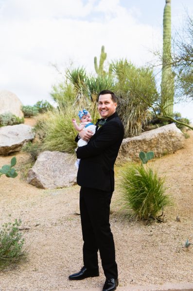 Groom posing with his daughter at a Clear acrylic, modern wedding table number with white flower and eucalyptus floral arrangement at a Troon north wedding reception by PMA Photography.