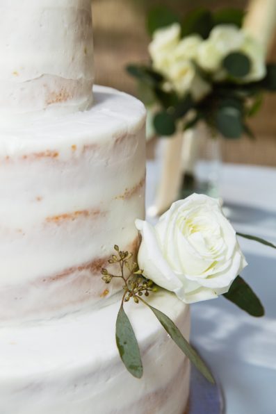 Simple white, three tiered wedding cake with rose and eucalyptus by PMA Photography.