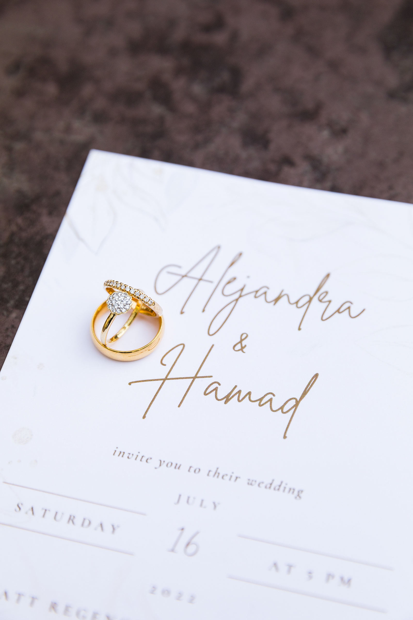 Couple's gold wedding rings on their simple, white and gold wedding invitations by PMA Photography.