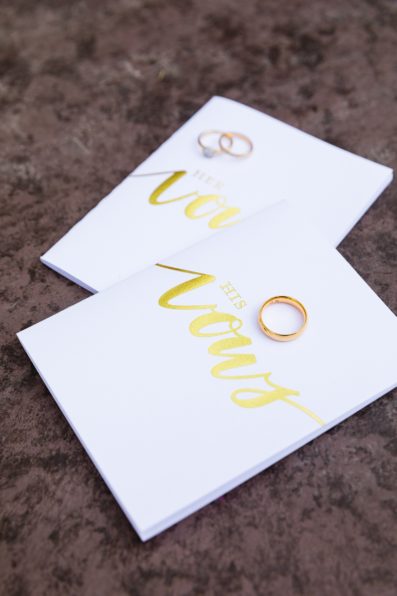 Couple's gold wedding rings on their simple, white and gold vow books by PMA Photography.