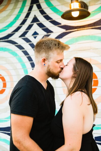 Adventurous couple share a kiss during their Roosevelt Row engagement session by Phoenix wedding photographer PMA Photography.