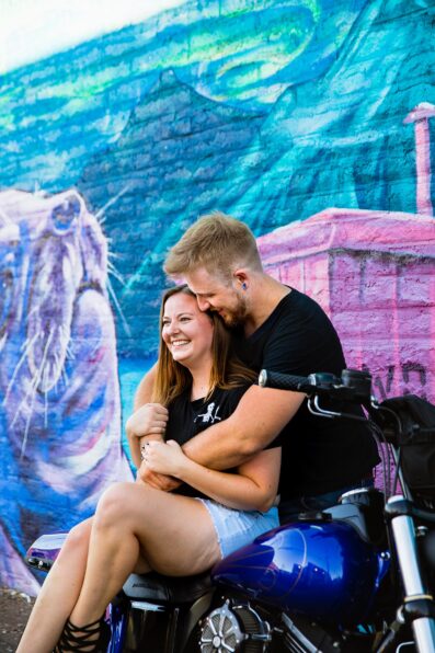 Adventurous couple laugh together on a motorcycle during their Phoenix engagement session by Arizona engagement photographer PMA Photography.