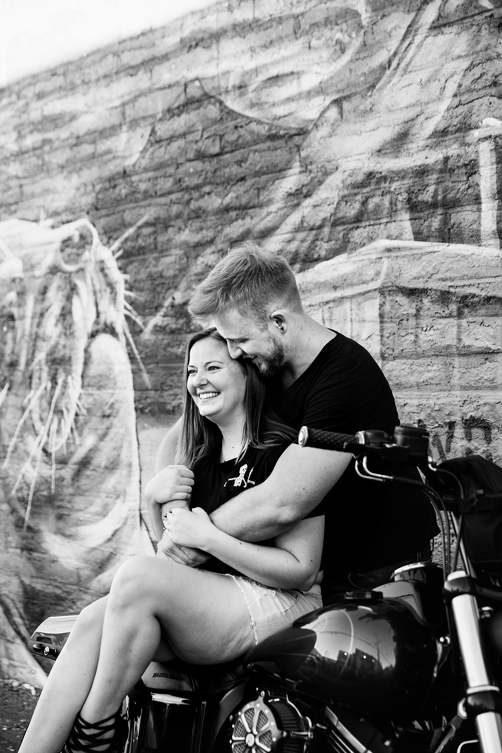 Adventurous couple laugh together on their motorcycle during their Phoenix engagement session by Arizona engagement photographer PMA Photography.