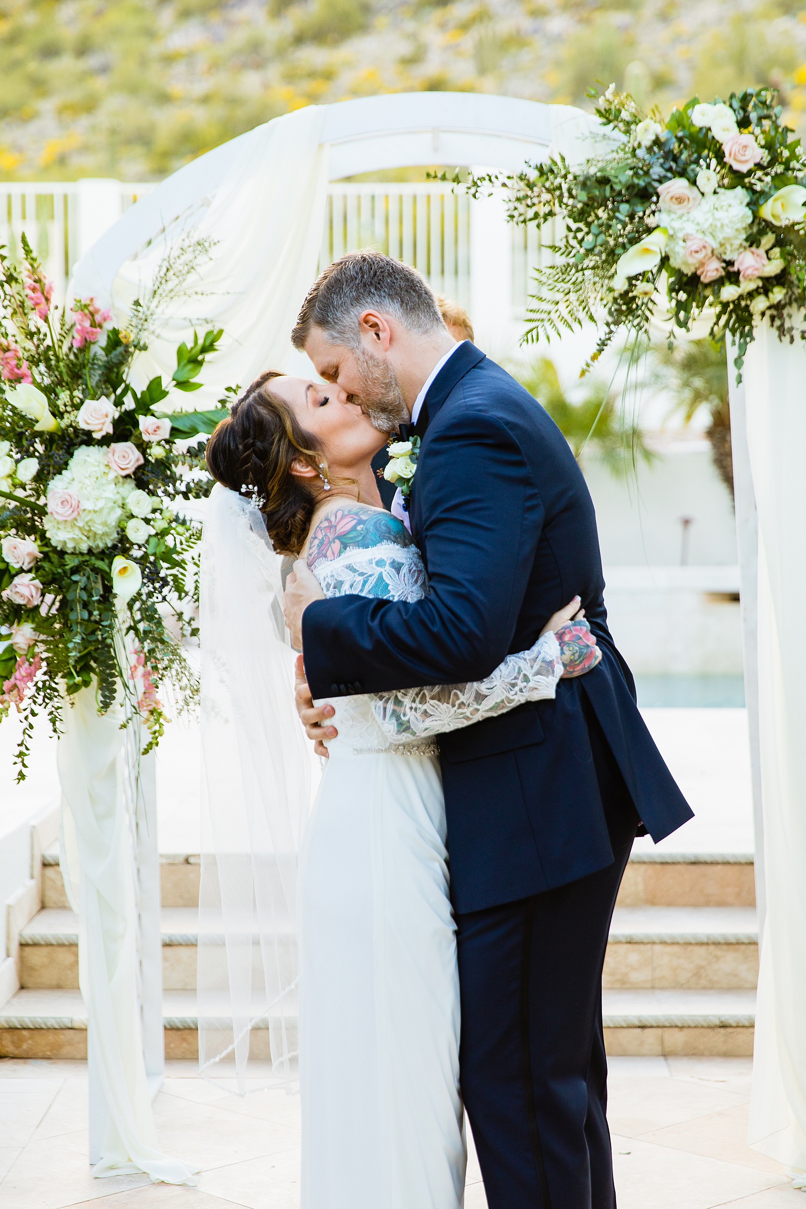 Bride and groom share their first kiss during their wedding ceremony at backyard by Arizona wedding photographer PMA Photography.