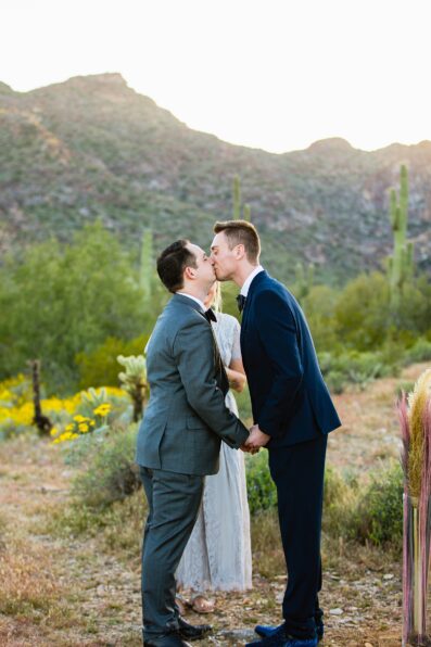 LGBTQ couple share their first kiss during their wedding ceremony at White Tanks by Arizona elopement photographer PMA Photography.