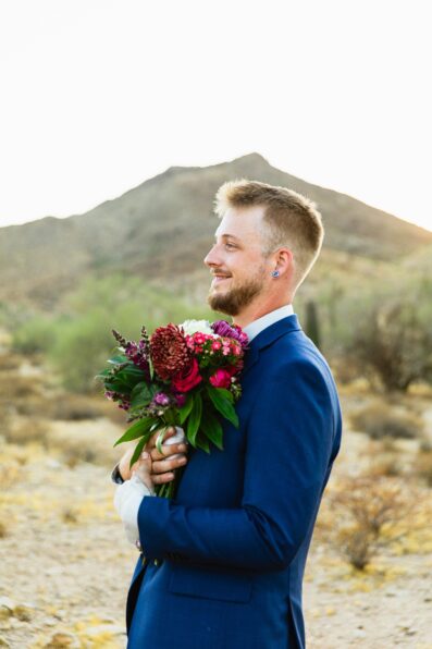 Groom holding vibrant bouquet by Juniper and Co Photography.