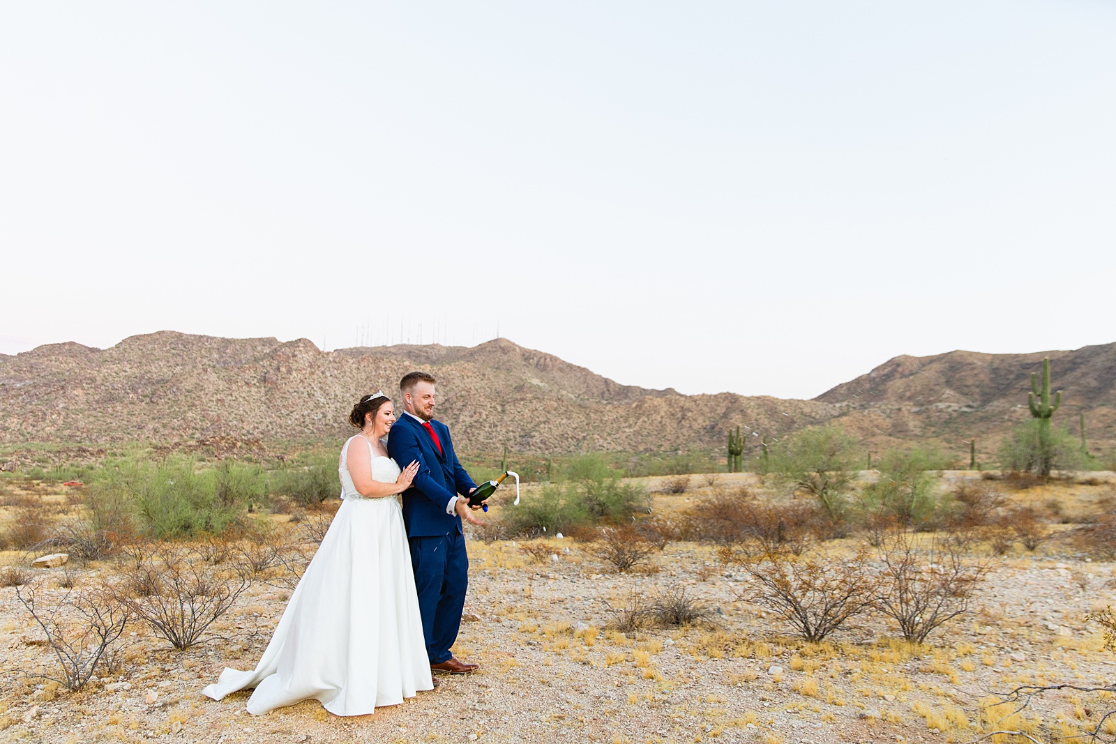 Bride and groom popping champagne together during their intimate desert wedding by Arizona wedding photographer Juniper and Co Photography.