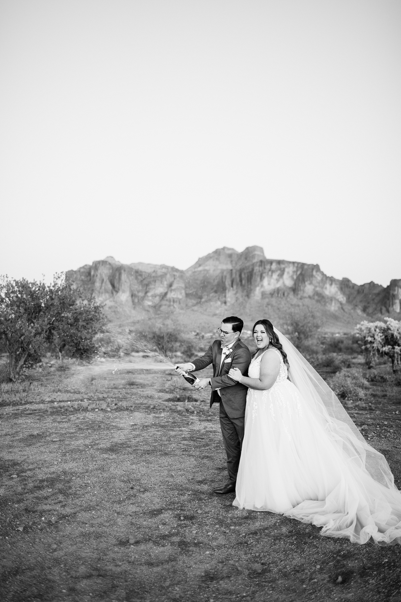 Bride & Groom popping champagne together during their a Phoenix desert intimate wedding by Arizona wedding photographer Juniper and Co Photography.