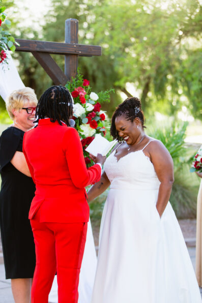 Same sex couple laughing together during their wedding ceremony at intimate desert by Phoenix wedding photographer Juniper and Co Photography.